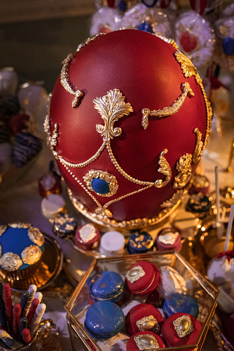 A Fabergé egg inspired cake, in deep red with ornate gold handpainted designs and a cake brooch feature